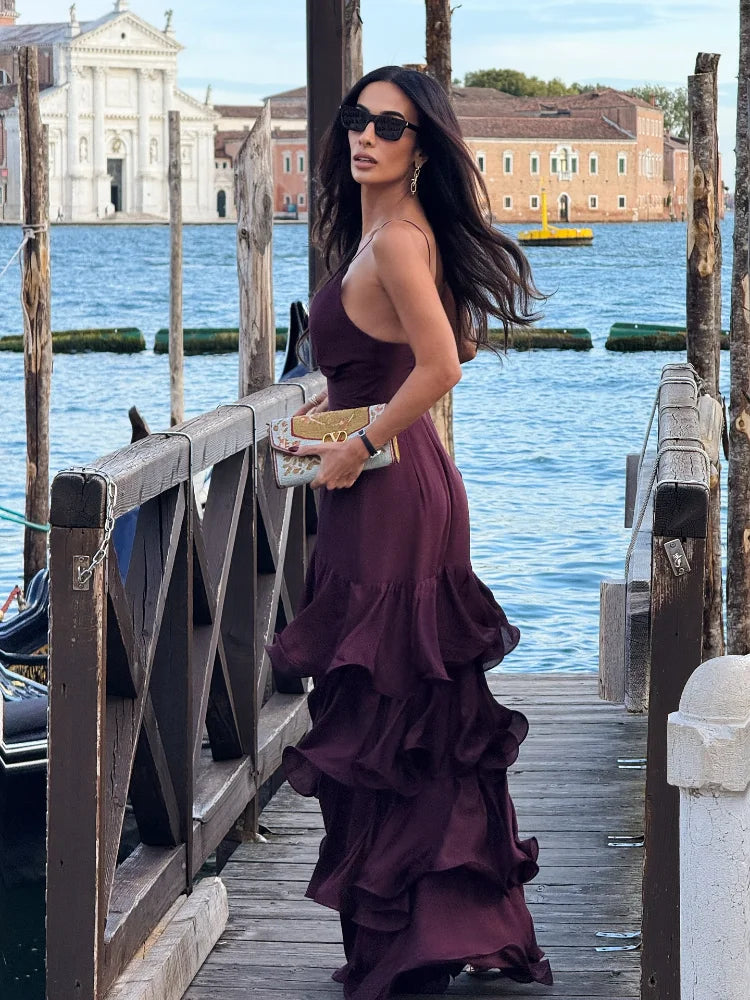 Woman in a purple dress standing on a wooden bridge by a waterfront with buildings in the background.