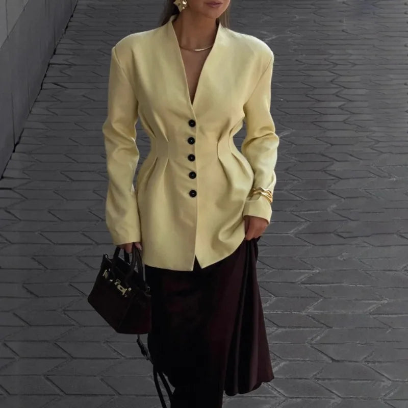 Person wearing a light yellow blazer with black buttons on a gray pavement background