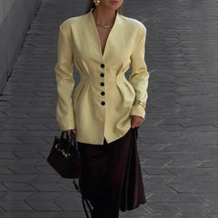 Person wearing a light yellow blazer with black buttons on a gray pavement background