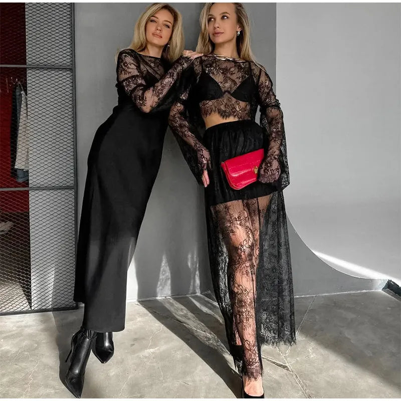 Two women in black lace outfits with a red handbag in an indoor setting.
