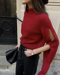 Person wearing a red sweater with cut-out design, holding a black clutch.