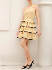 Woman wearing a yellow dress with black trim against a white wall