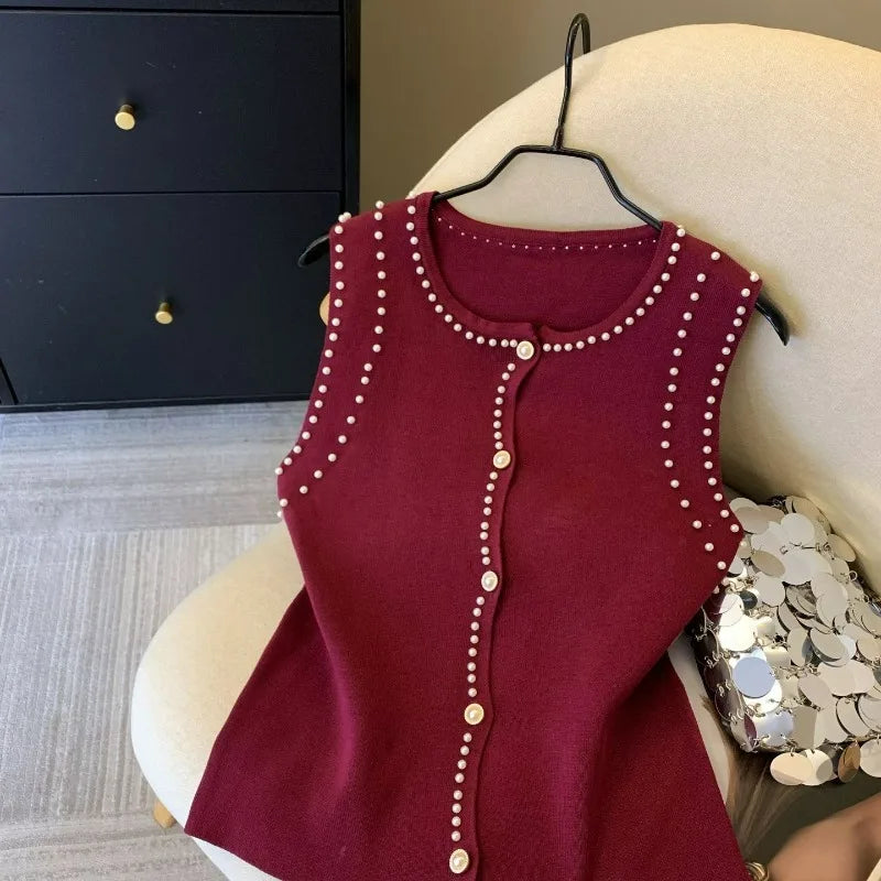Red sleeveless top with pearl embellishments on a hanger against a neutral background
