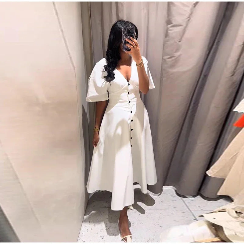 Woman taking a mirror selfie wearing a white dress in a fitting room.