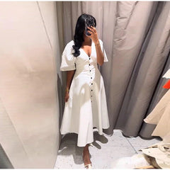 Woman taking a mirror selfie wearing a white dress in a fitting room.