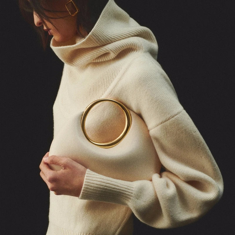 Person wearing a cream-colored sweater with a gold ring clutch.