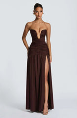 Woman wearing a strapless brown evening gown with a high slit on a white background