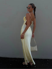 Woman in a white dress with floral details, holding a white handbag against a plain background