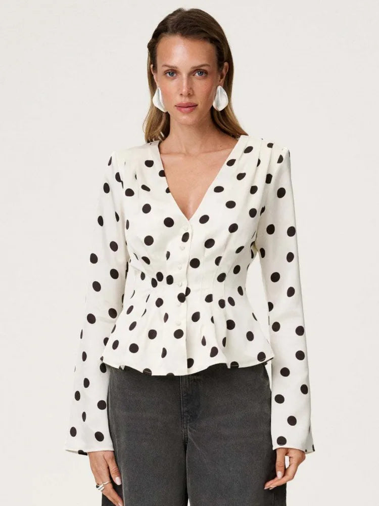 Woman wearing a white blouse with black polka dots on a plain background