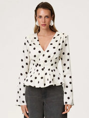 Woman wearing a white blouse with black polka dots on a plain background