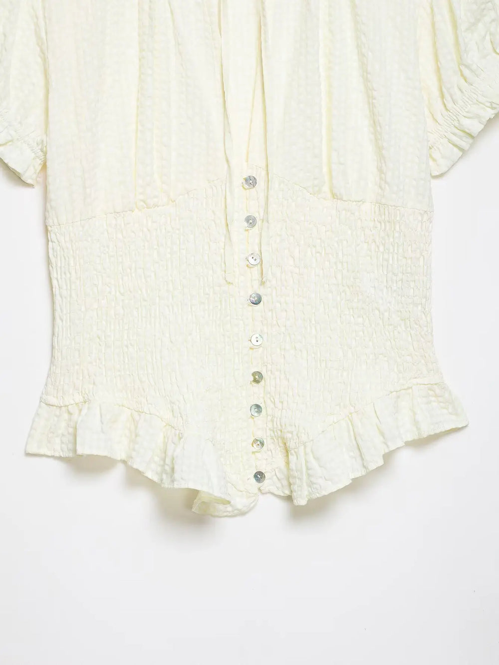 Close-up of a cream-colored blouse with ruffled details on a white background