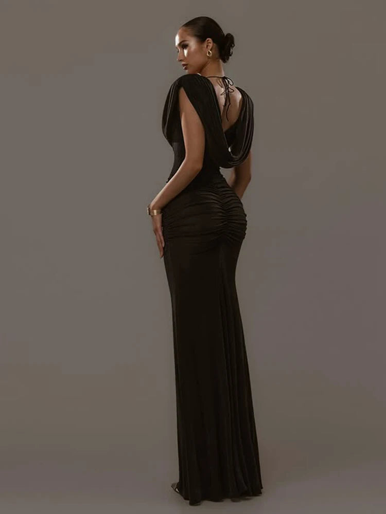 Woman wearing a black evening gown with a deep neckline and ruched details on a plain background