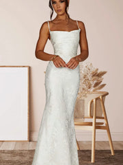 Woman wearing a white lace dress in a room with a wooden chair and decorative elements.