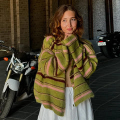 Woman wearing a green and pink striped sweater standing in front of motorcycles.