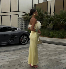 Woman in a yellow dress standing next to a car with a modern building and plants in the background