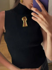 Person wearing a black sleeveless top with a gold keyhole brooch, holding a phone to their ear.