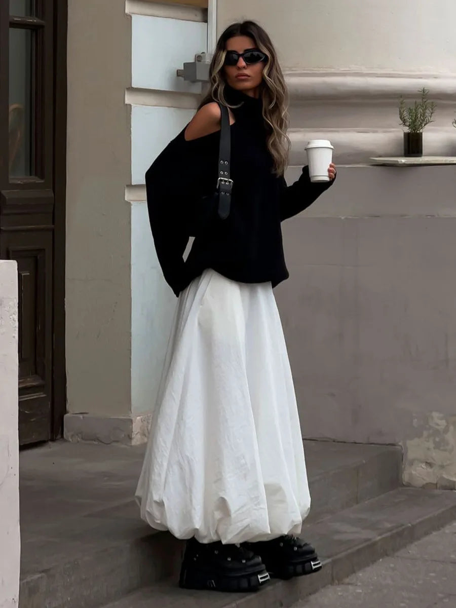 Woman in black top and white skirt holding a coffee cup on steps.