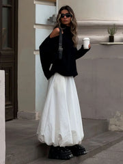 Woman in black top and white skirt holding a coffee cup on steps.
