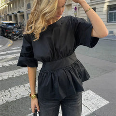 Woman wearing a black peplum top and dark pants on a city street.