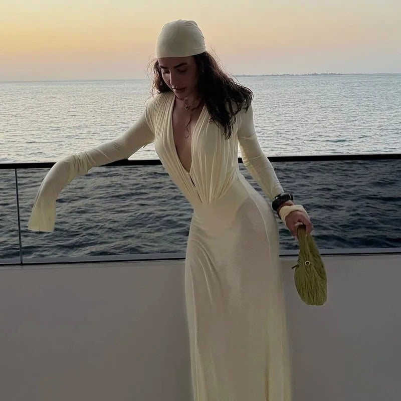 Woman in a white dress and headscarf standing by the water at sunset