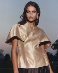 Woman wearing a gold satin top with a blurred outdoor background