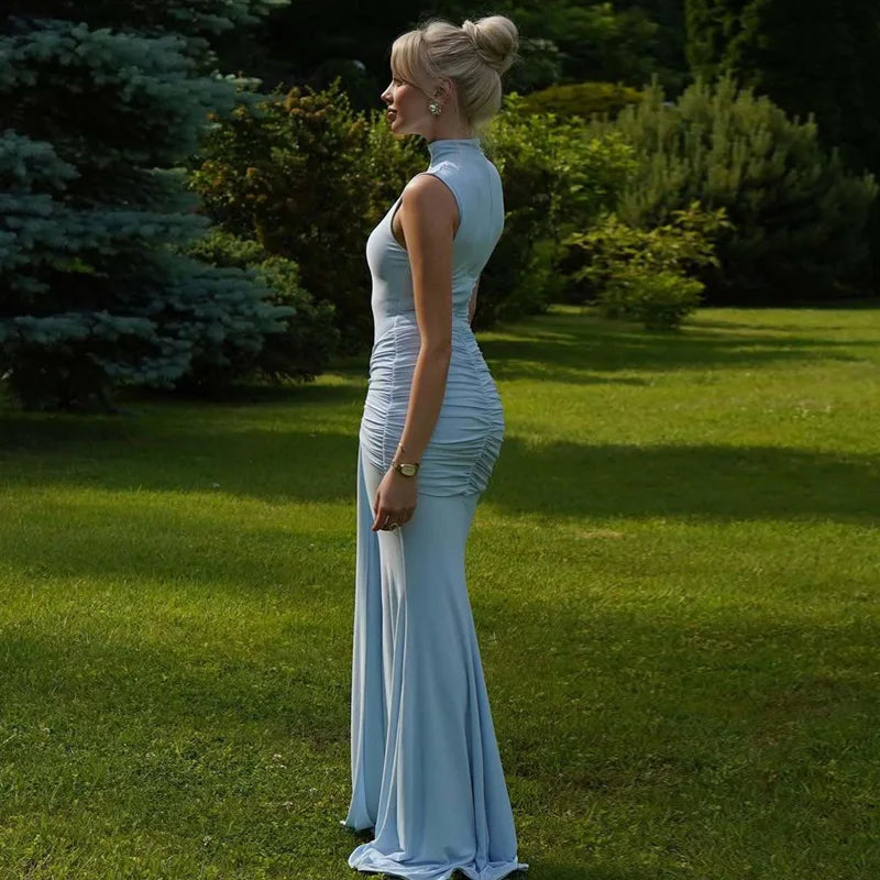 Woman in a light blue evening gown standing on grass with trees in the background