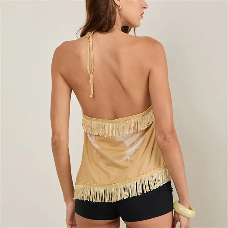 Woman wearing a beige halter top with fringe details and black shorts on a plain background