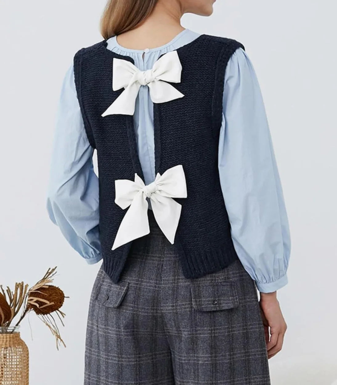 Person wearing a navy vest with white bows and a light blue shirt on a plain background