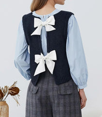 Person wearing a navy vest with white bows and a light blue shirt on a plain background