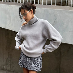 Woman wearing a light gray sweater and leopard print skirt against a concrete wall.