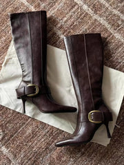 Close-up of pointed toe stiletto heel knee high boots with buckle.