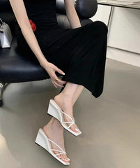 Person wearing a black dress and white wedge sandals sitting on a chair.