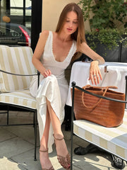 Woman in a white dress sitting on a bench with a brown bag next to her.