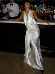 Person in a white satin dress standing behind a bar with bottles in the background