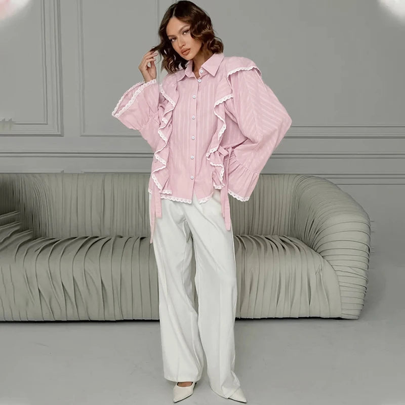 Woman wearing a pink ruffled blouse and white pants in a room with a gray sofa.