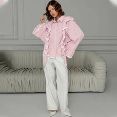 Woman wearing a pink ruffled blouse and white pants in a room with a gray sofa.
