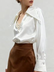 Person wearing a white blouse with a pearl necklace and brown skirt on a plain background