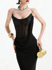 Woman wearing a black strapless dress with gold accents, holding a gold clutch against a white background.