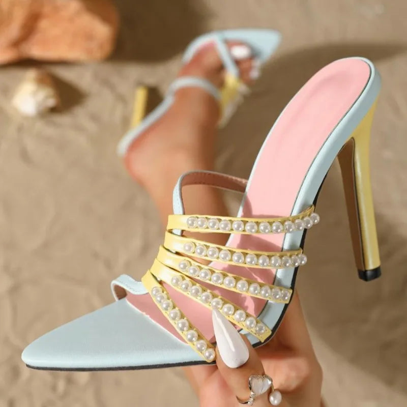 Close-up of a hand holding beaded strappy pointed toe heeled mules.