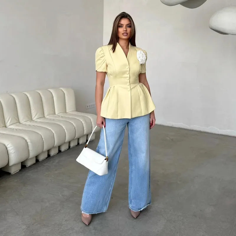 Woman in a yellow peplum top and blue jeans standing in a room with a beige sofa.