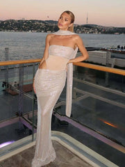 Woman in a sparkling evening gown standing on a balcony with a waterfront view.
