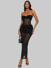 Woman wearing a black strapless top and sheer black skirt on a gray background