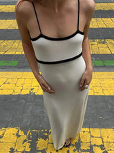 Person wearing a white dress with black straps on a yellow and black checkered floor.