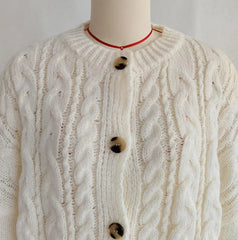 White cable knit cardigan on a mannequin with a plain background