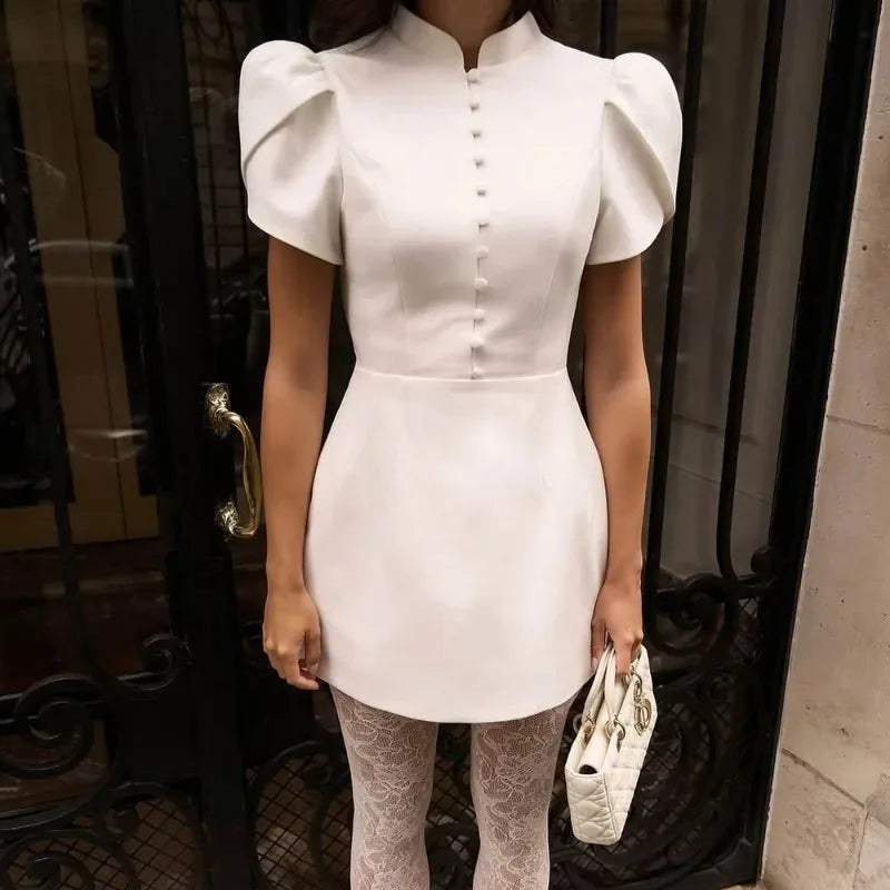 Person wearing a white dress with puffed sleeves in front of a door.