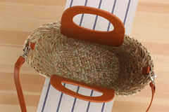 Woven handbag with orange handle on a striped fabric background