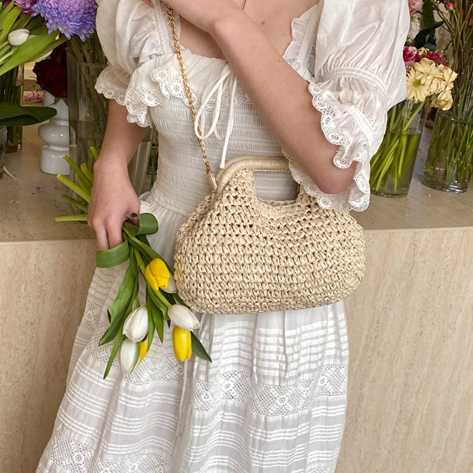 Person holding a woven handbag and flowers in a decorated indoor setting