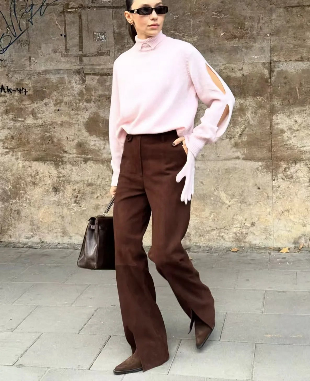 Person wearing a pink blouse and brown pants against a textured wall.