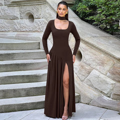 Woman in a brown dress standing on stone steps with a stone wall and greenery in the background