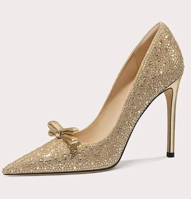 Gold high-heeled shoe with decorative bow on a white background